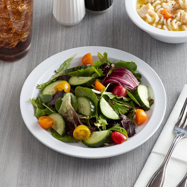 An Acopa white melamine plate with salad on a wood table.
