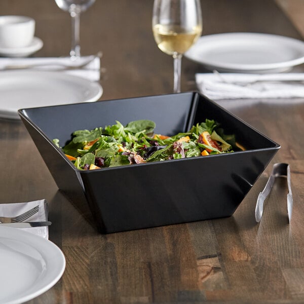 A black square melamine bowl filled with salad on a table.