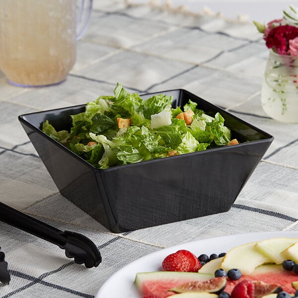A table with a black Acopa Rittenhouse melamine bowl filled with salad and fruit.