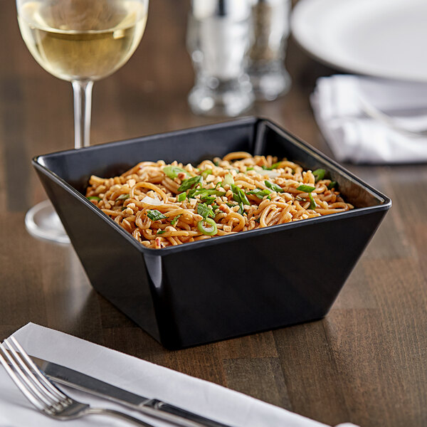 A black Acopa Rittenhouse melamine bowl filled with noodles, green onions, and peanuts on a table with a glass of white wine.