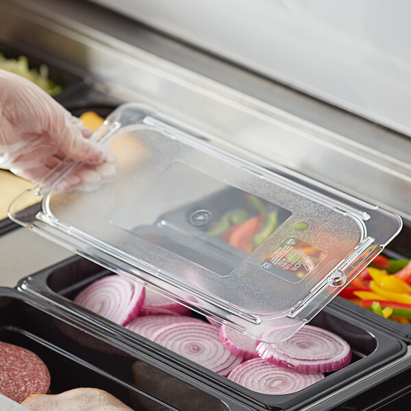 A person in a white glove is holding a Vigor clear plastic lid over food in a plastic container.
