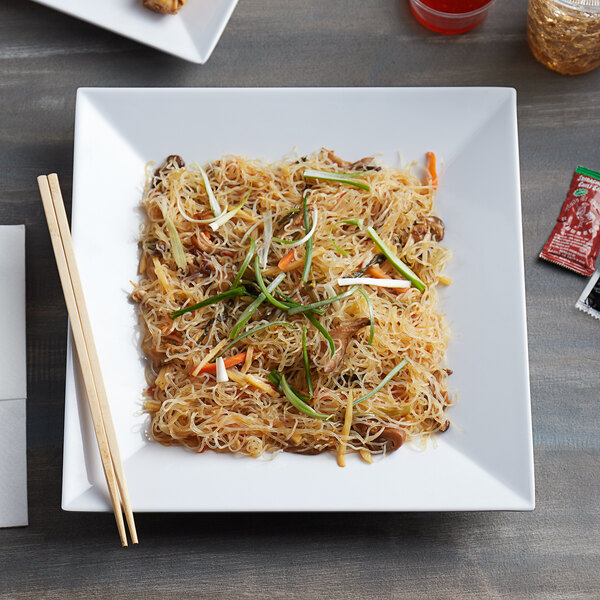 A white square melamine plate with noodles and vegetables with chopsticks.