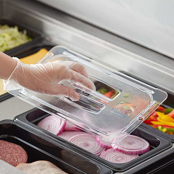 A person in a glove using a Vigor clear plastic lid to cover food in a plastic container.