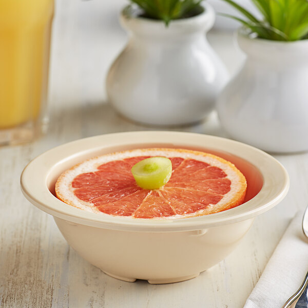 A bowl of fruit with a slice of grapefruit on top sitting on a table.