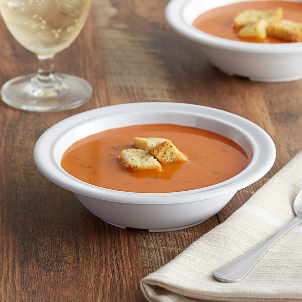 A white narrow rim melamine bowl of soup with croutons on a napkin next to a glass of wine.