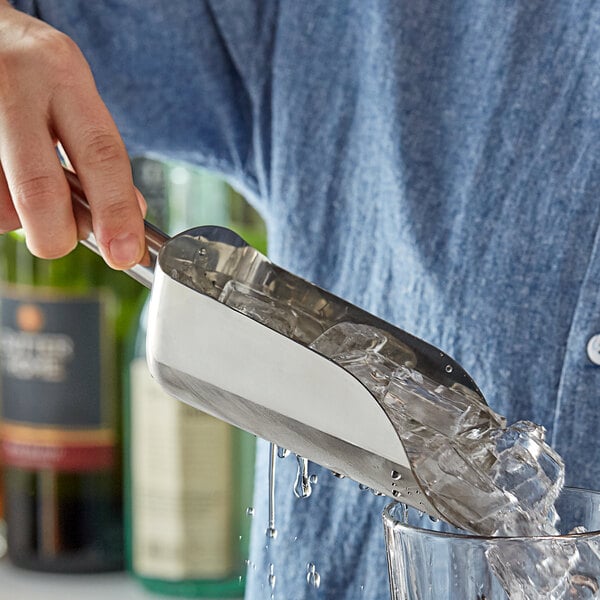 A person using a Tablecraft stainless steel ice scoop to add ice to a glass.
