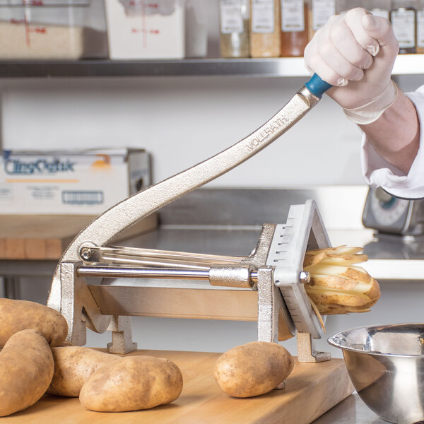 A person using a Vollrath French fry cutter to cut potatoes on a counter.