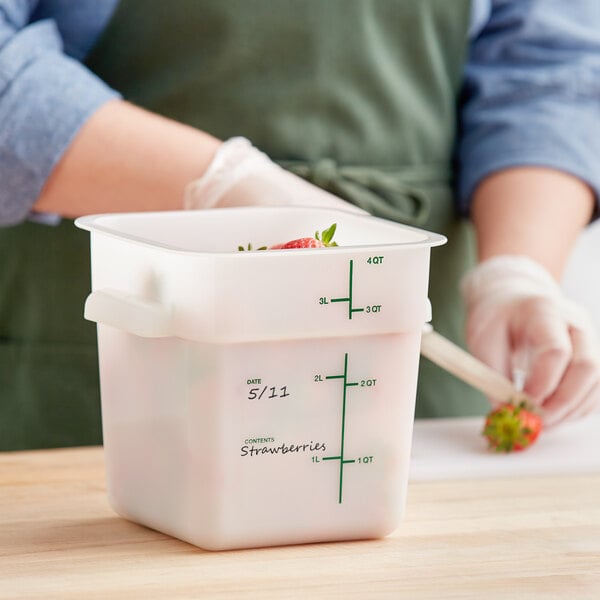 A person in a green apron cutting strawberries inside a white Vigor square plastic container.