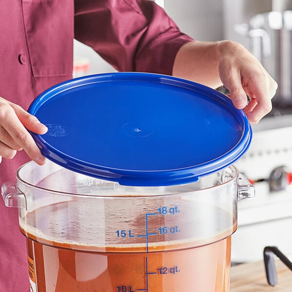 A person holding a blue Vigor food storage container lid over a large pot of brown liquid.