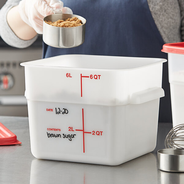A person using a measuring cup to pour brown sugar into a white Vigor food storage container.