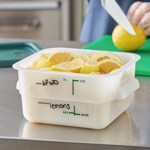 A woman cutting lemons into a Vigor white square food storage container on a school kitchen counter.