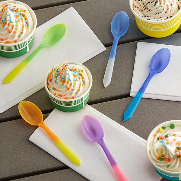 A table with assorted color-changing plastic spoons next to cups of ice cream with sprinkles.