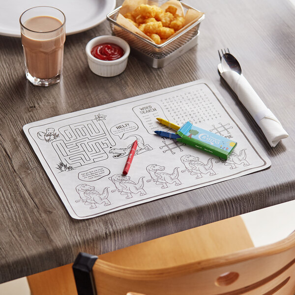 A wooden table with a Choice Kids Dinosaur Interactive Placemat and a bowl of food, a glass of milk, and a spoon wrapped in a napkin.