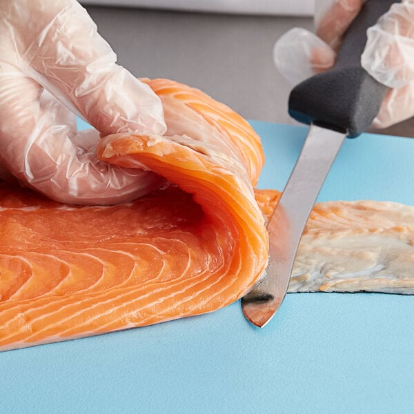 A person's gloved hand using a Mercer Culinary semi-flexible fillet knife to cut a piece of salmon.