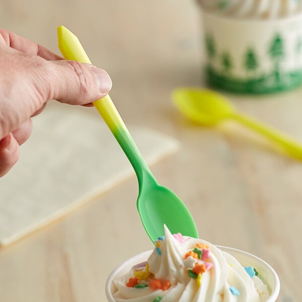 A hand holding a yellow and green color-changing dessert spoon over a cup of ice cream.