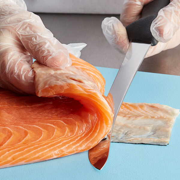 A gloved hand using a Mercer Culinary semi-flexible fillet knife to cut salmon.