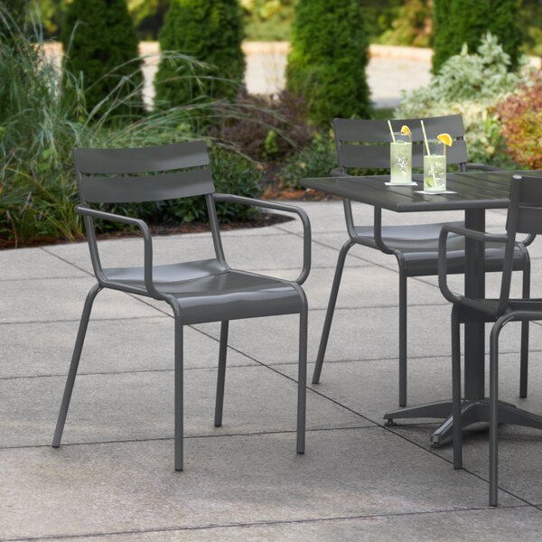 A Lancaster Table & Seating matte gray aluminum outdoor arm chair on a patio with drinks.