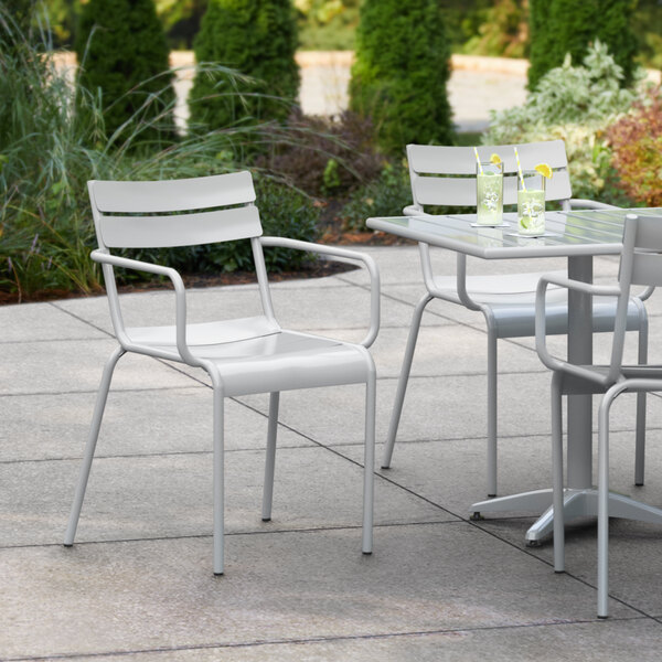 A white Lancaster Table & Seating outdoor arm chair with a glass of water on a table.