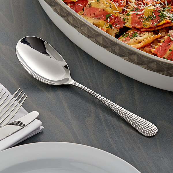 An Acopa stainless steel serving spoon next to a dish of pasta.