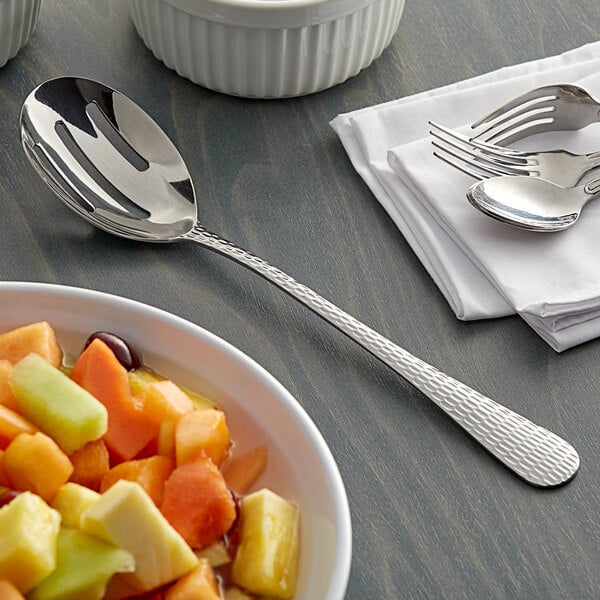 An Acopa stainless steel slotted serving spoon in a bowl of fruit salad on a table.