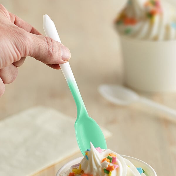 A hand holding a green Pearl to Green color-changing dessert spoon over a cup of ice cream.