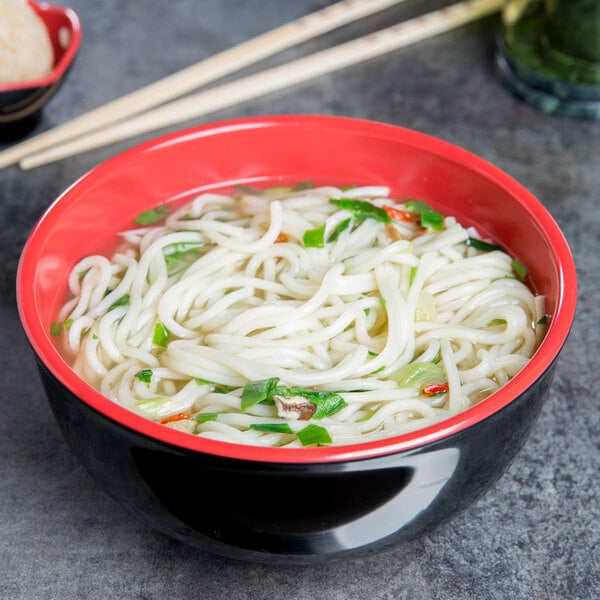 A melamine bowl filled with noodles and vegetables with chopsticks.