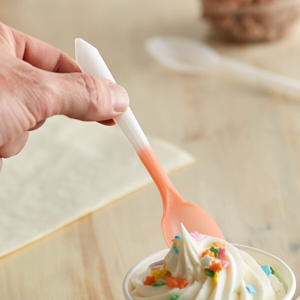 A hand holding a Pearl to Orange color-changing dessert spoon over a bowl of ice cream.