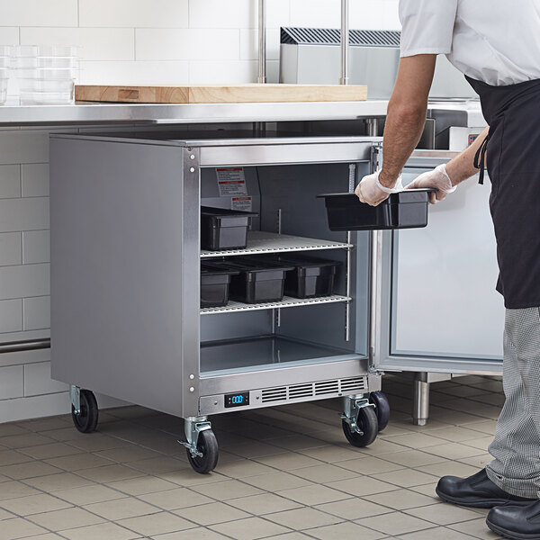 A man in a white shirt and black pants opening a Beverage-Air undercounter freezer in a school kitchen.