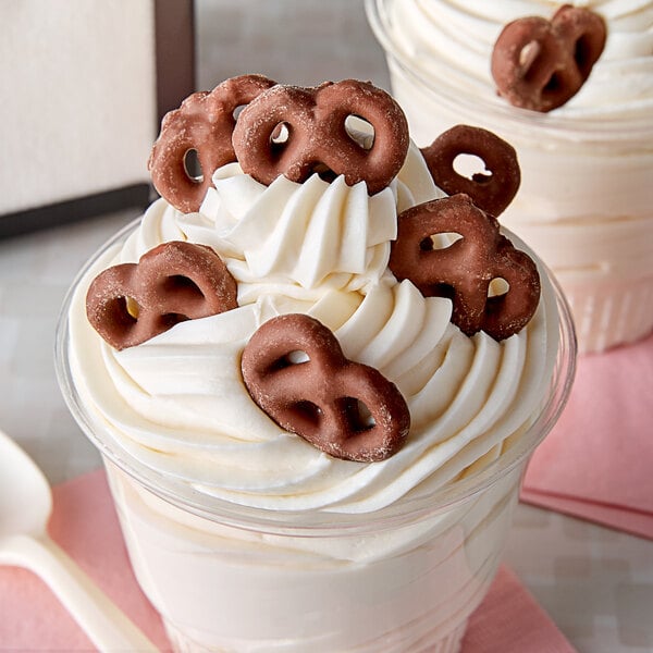 A cup of ice cream with chocolate glazed pretzels on top.
