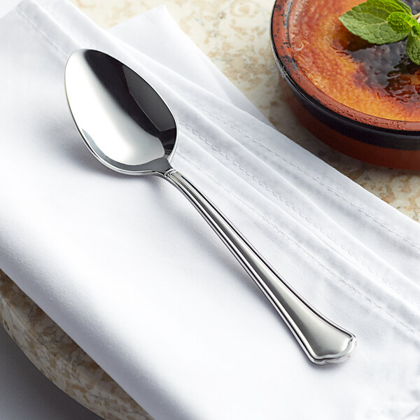 An Acopa Sienna stainless steel dinner spoon on a napkin next to a bowl of creme brulee.