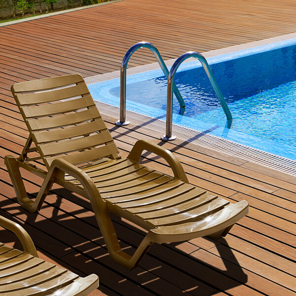 A Lancaster Table & Seating sand resin chaise lounge on a pool deck.