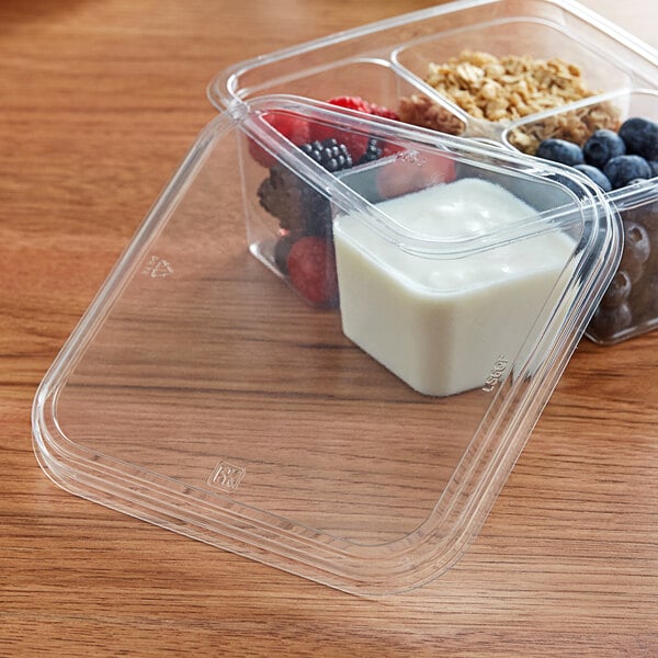 A clear Fabri-Kal plastic deli container filled with yogurt, berries, and granola.