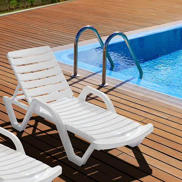 Two white Lancaster Table & Seating adjustable resin chaise lounges next to a pool.