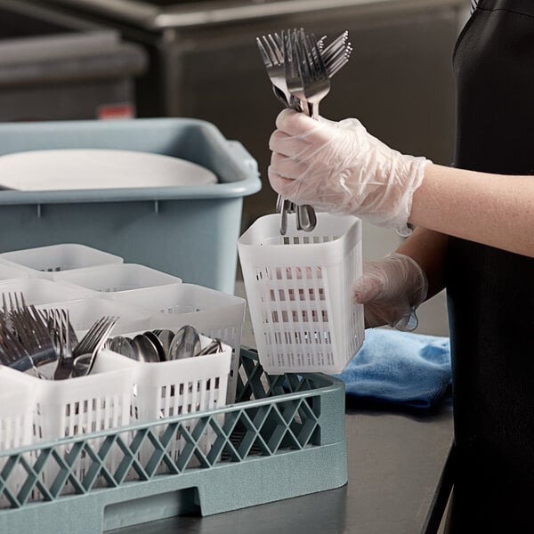 A person in a black apron putting silverware into a white plastic basket with holes.
