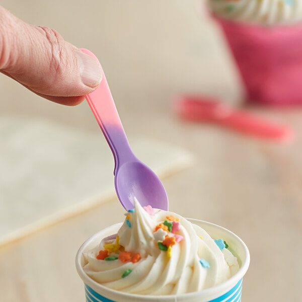 A hand holding a pink to purple color-changing tasting spoon over a cup of ice cream.