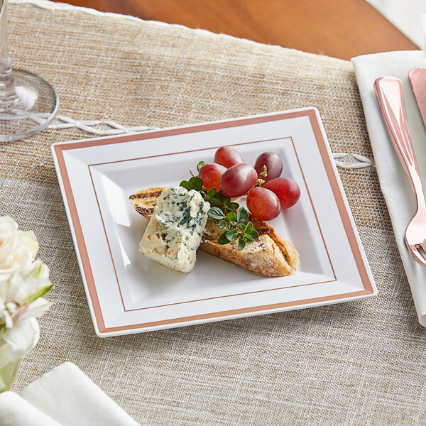 A Visions white plastic plate with rose gold and copper bands holding food on a table with a fork and knife.