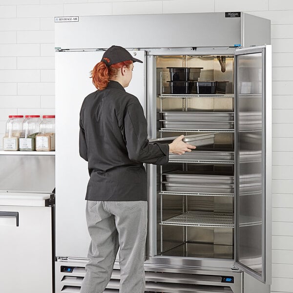 A woman opening a Beverage-Air Horizon Series refrigerator in a professional kitchen.