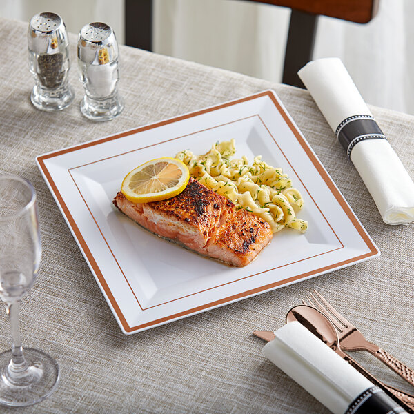 A Visions white plastic plate with rose gold and copper bands holding food with a lemon wedge on a table.