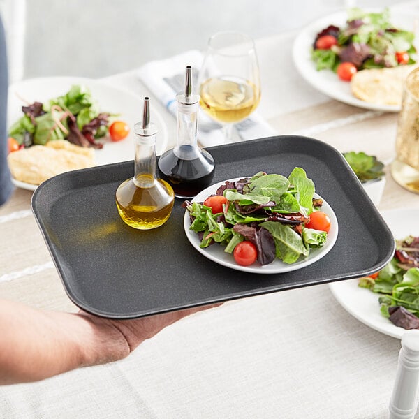 A person holding a Choice black rectangular non-skid serving tray with salad and tomatoes.