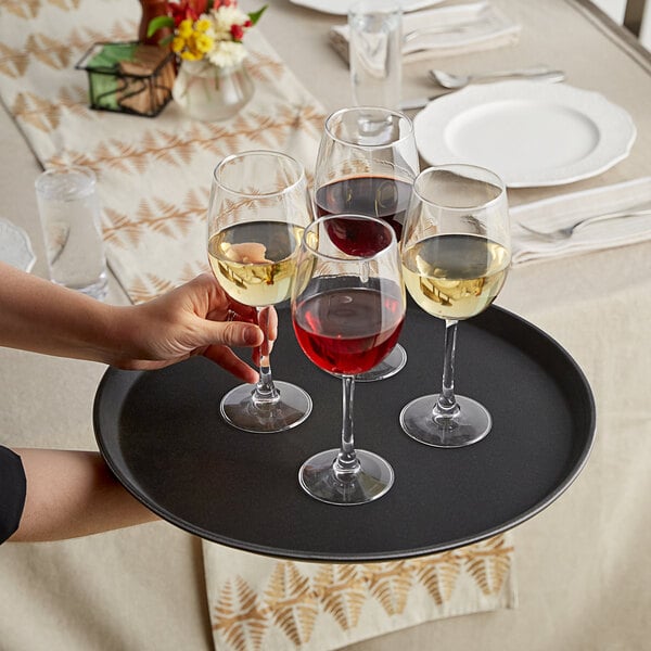 A person holding a Choice black non-skid serving tray with glasses of red and white wine.