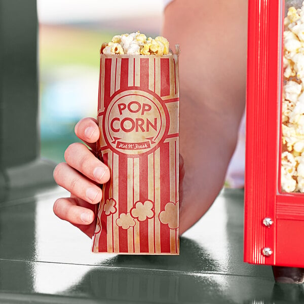 A hand holding a red and white striped Carnival King popcorn bag.