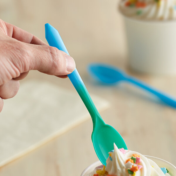 A hand holding a blue spoon over a cup of ice cream.