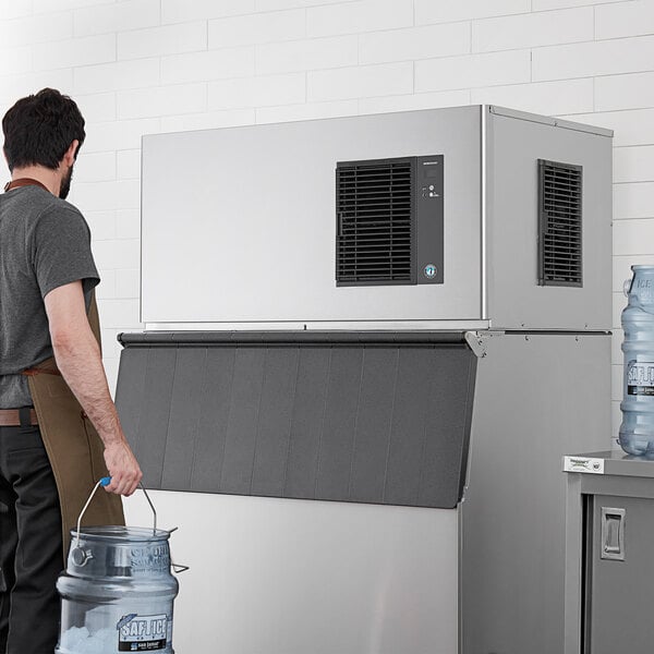 A man wearing a brown apron pouring water into a large Hoshizaki air cooled ice machine.