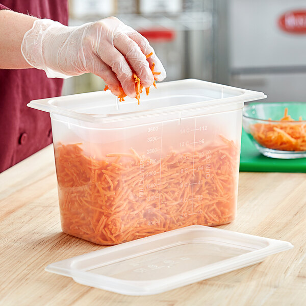 A person in gloves putting carrots in a San Jamar translucent plastic food container.