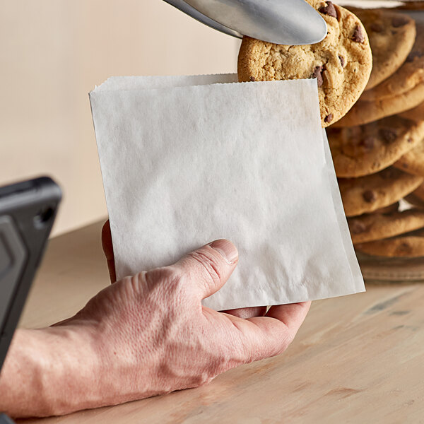 A hand holding a Choice white paper bag with a cookie inside.