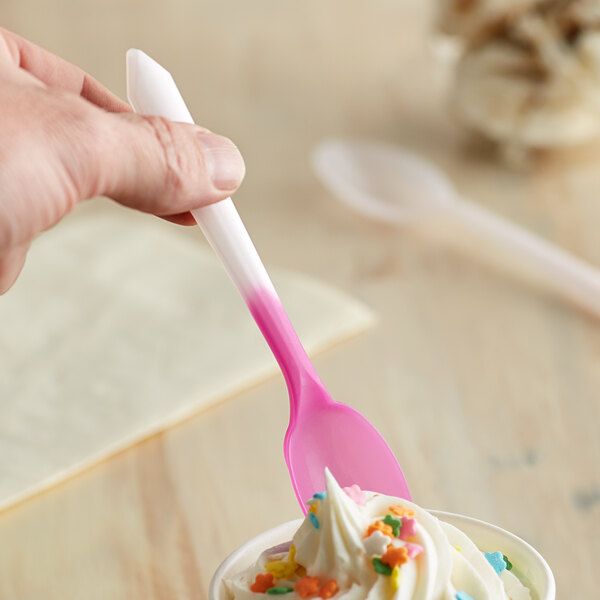 A hand holding a Pearl to Pink color-changing dessert spoon over a cup of ice cream.