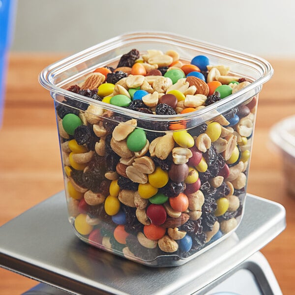A plastic Fabri-Kal deli container of nuts and candies on a scale.