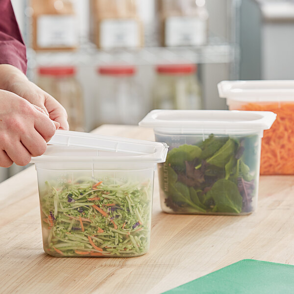 A person's hand putting shredded cabbage and carrots in a San Jamar translucent plastic food container.