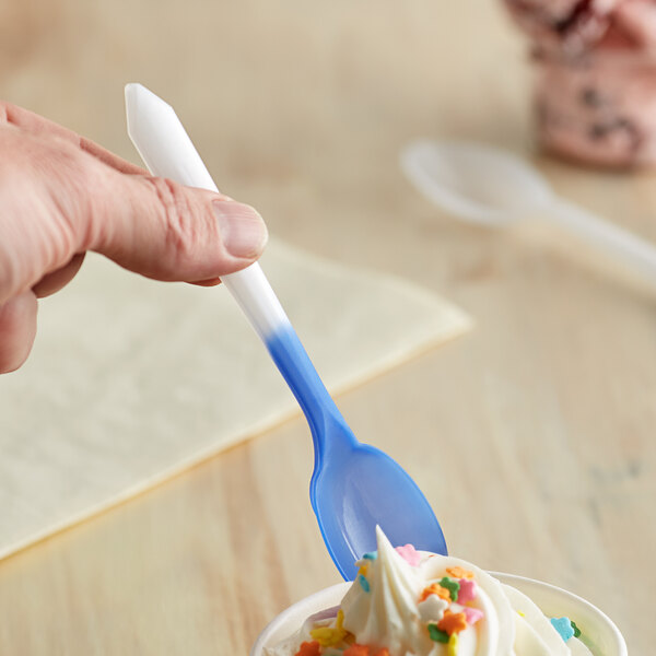 A hand holding a Pearl to Blue color-changing dessert spoon over a cup of ice cream.