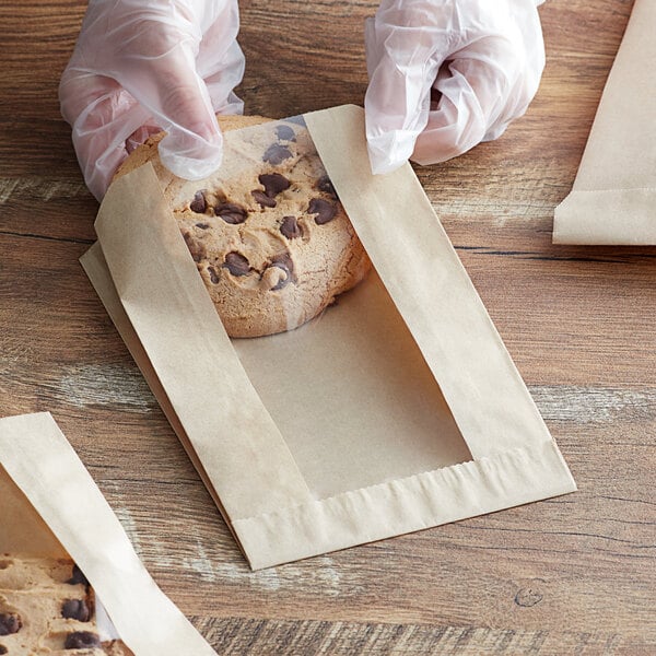 A person in gloves holding a cookie in a Choice kraft paper bag.